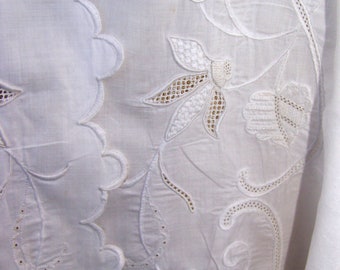 May include: White cotton fabric with intricate embroidered floral designs. The fabric has a scalloped edge and is delicate and lacy.