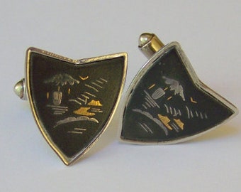 May include: A pair of silver cufflinks with black enamel and gold accents. Each cufflink features a stylized design of a landscape with a tree and a building.