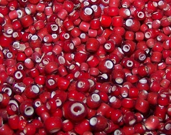 May include: A bowl filled with red and white glass beads. The beads are small and round, with a white center and a red outer layer.