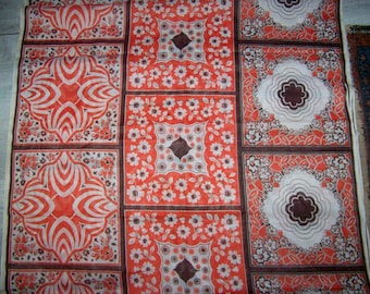 May include: A red and white fabric with a repeating pattern of geometric shapes and floral designs. The fabric has a brown border.