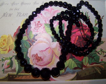 May include: A strand of black faceted glass beads, arranged in a circle on a vintage floral card with the text "With Best Wishes for the New Year".