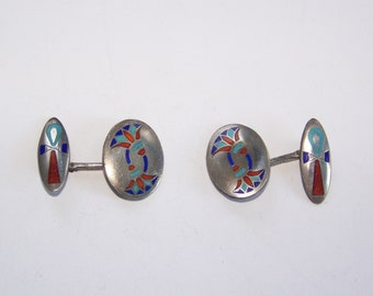 May include: A pair of silver cufflinks with enamel detailing. One cufflink features a blue, red, and turquoise design, while the other features an ankh symbol in red, blue, and turquoise.