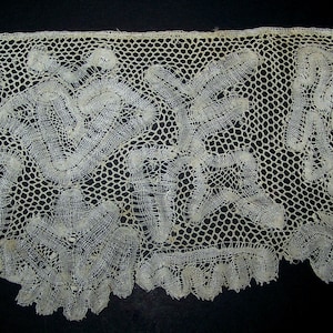 Op de afbeelding: Een delicate witte kantversiering met een bloemenpatroon. De kant is gemaakt van fijne draden en heeft een delicaat, ingewikkeld ontwerp.