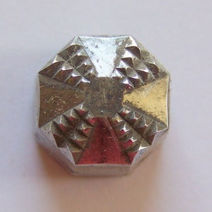 May include: A silver-colored, octagonal-shaped metal button with a textured, geometric design.