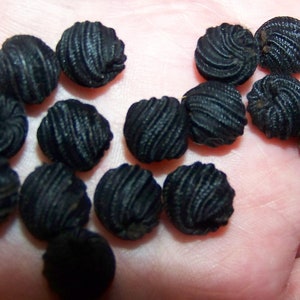 May include: A collection of black fabric covered buttons with a swirl design.