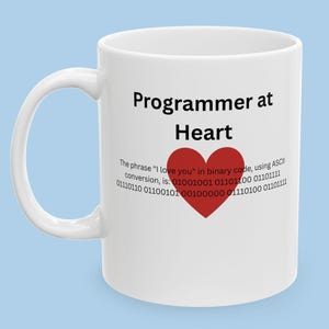 May include: White ceramic mug with a red heart and the text "Programmer at Heart". The text below the heart reads "The phrase "I love you" in binary code, using ASCII conversion, is: 01001001 01101100 01101111 01110110 01100101 00100000 01110100 01101111".