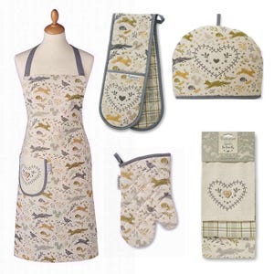 May include: A set of kitchen textiles with a woodland design. Includes an apron, oven mitt, double oven glove, tea cosy, and tea towels. The items have a cream background with foxes, birds, and heart motifs.