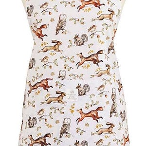 May include: White apron featuring a woodland animal print with foxes, owls, squirrels, and rabbits. The apron has a green strap and a pocket. The apron is displayed on a mannequin.