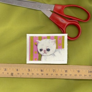 May include: A white cat with pink and green stripes in the background. The cat has a sad expression and is looking to the left.