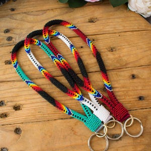 Op de afbeelding: Drie kralen sleutelhangers met kleurrijke geometrische patronen in rood, wit, zwart en turquoise. De sleutelhangers zijn bevestigd aan zilveren sleutelringen.