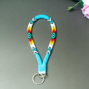 May include: A beaded key chain with a blue, white, red, and yellow geometric pattern. The key chain has a silver key ring.