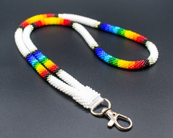 Op de afbeelding: Een kralenkoord met een regenboogpatroon en witte kralen. Het heeft een zilveren draaiknoop.