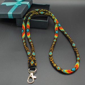 May include: A black beaded lanyard with a geometric pattern in yellow, orange, and blue. The lanyard has a silver clip on one end.