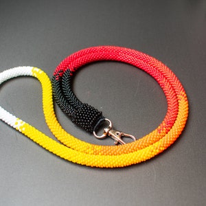 May include: A beaded lanyard with a black, yellow, orange, and red color gradient. The lanyard has a silver metal clasp.