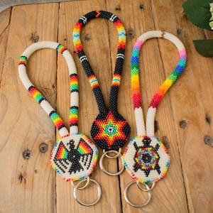 May include: Three beaded keychains with colorful designs. Each keychain features a different design: a bird, a star, and a turtle. The keychains are made with small, colorful beads and have a metal ring for attaching keys.