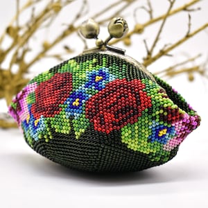 以下が含まれることがあります： 花柄のビーズの小銭入れ。小銭入れは、花柄を形成する赤、青、緑、ピンクのビーズが付いた濃い緑色の背景が特徴です。留め金はブロンズ色です。