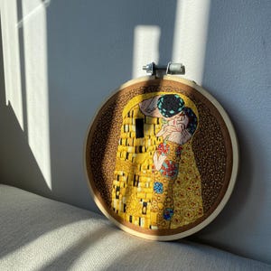Pu&ograve; includere: Opera ricamata in un cerchio di legno che rappresenta un famoso dipinto di due figure che si baciano. L'opera &egrave; realizzata in stile mosaico con filo giallo, oro e blu.