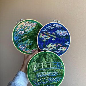 May include: Three round embroidery hoops featuring water lily scenes. The hoops have a green border and a wooden frame. The embroidery depicts colorful water lilies and foliage in shades of blue, pink, and green.
