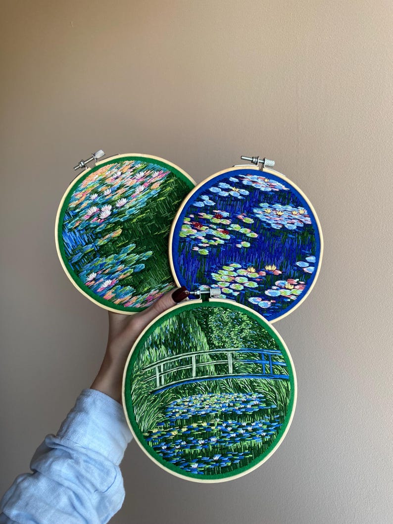 May include: Three round embroidery hoops featuring water lily scenes. The hoops have a green border and a wooden frame. The embroidery depicts colorful water lilies and foliage in shades of blue, pink, and green.