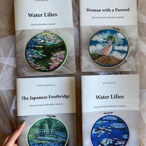 May include: Four hand embroidery tutorial booklets. The covers feature colorful embroidered art within wooden hoops. Titles include "Water Lilies," "Woman with a Parasol," and "The Japanese Footbridge." The booklets are on a light background.