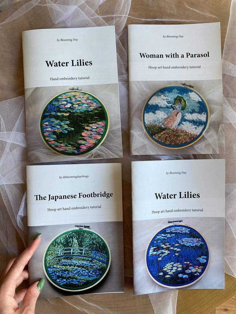 May include: Four hand embroidery tutorial booklets. The covers feature colorful embroidered art within wooden hoops. Titles include "Water Lilies," "Woman with a Parasol," and "The Japanese Footbridge." The booklets are on a light background.