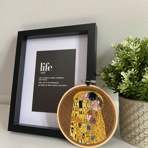 Pu&ograve; includere: Una stampa incorniciata con il testo "life is made of small moments like these. Find joy in the ordinary. Do more of what makes you happy." Un cerchio da ricamo circolare con una rappresentazione a perline del dipinto di Gustav Klimt "Il Bacio".