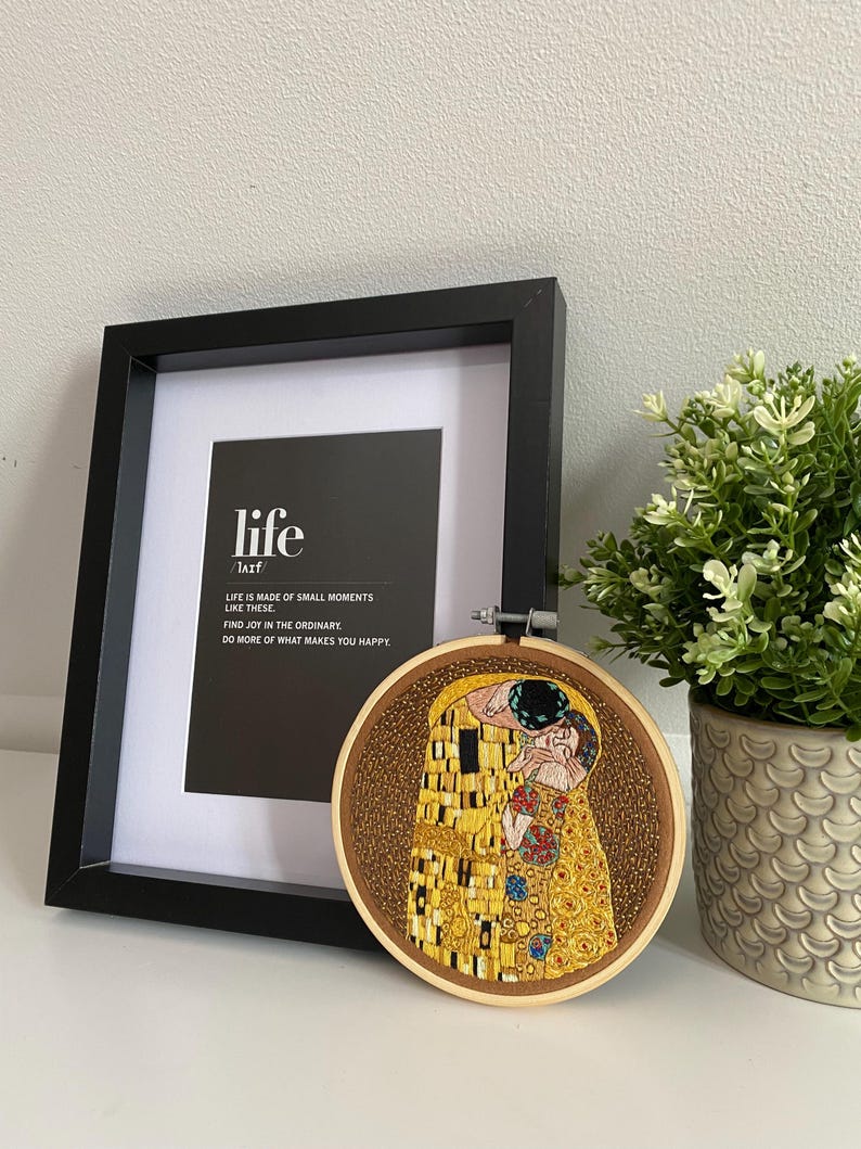 Pu&ograve; includere: Una stampa incorniciata con il testo "life is made of small moments like these. Find joy in the ordinary. Do more of what makes you happy." Un cerchio da ricamo circolare con una rappresentazione a perline del dipinto di Gustav Klimt "Il Bacio".
