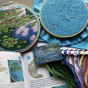 May include: Two embroidery hoops with floral designs, one completed and one in progress. The finished piece features pink and green foliage. A card with a Claude Monet quote and embroidery floss in various colors are also visible.
