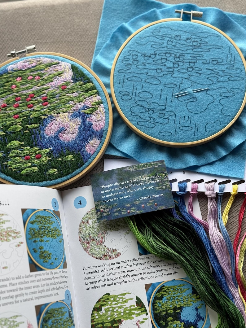 May include: Two embroidery hoops with floral designs, one completed and one in progress. The finished piece features pink and green foliage. A card with a Claude Monet quote and embroidery floss in various colors are also visible.