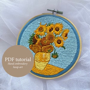 Może przedstawiać: Ręcznie haftowany obręcz z motywem bukietu słoneczników w żółtym wazonie. Haftowany na niebieskim materiale z jasnoniebieskim tłem.