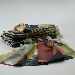 Può includere: Una pila di quadrati di tessuto con un motivo floreale colorato. Il tessuto è piegato e legato insieme con uno spago. Il tessuto è disposto su una superficie bianca.