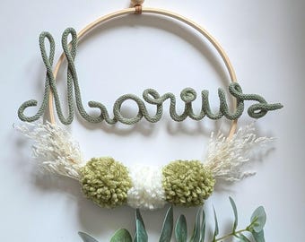 Knitted name wreath with pom-poms and dried flowers for decorating a baby's or child's room, perfect as a gift for a birth, christening, or birthday.