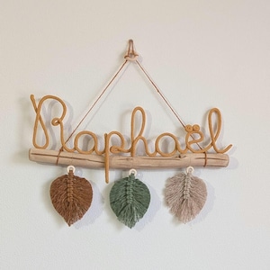 Personalisierter gestrickter Name auf Treibholz mit Makramee-Verzierung, Regenbogen und Blättern, Wanddekoration für ein Kinderzimmer