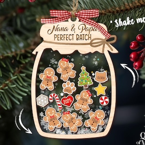 May include: Wooden Christmas ornament shaped like a jar, with the words "Nana & Papa's PERFECT BATCH" on top. Inside, gingerbread men and other festive shapes float. A red and white checkered ribbon is attached for hanging.