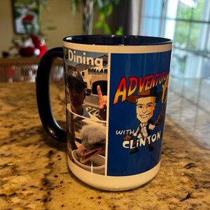 Puede incluir: Una taza de cer&aacute;mica grande con interior y asa azules. La taza presenta un collage de im&aacute;genes y las palabras "Dining Dollar" y "Adventures with Clinton" en un dise&ntilde;o colorido. La taza est&aacute; sobre una encimera moteada.