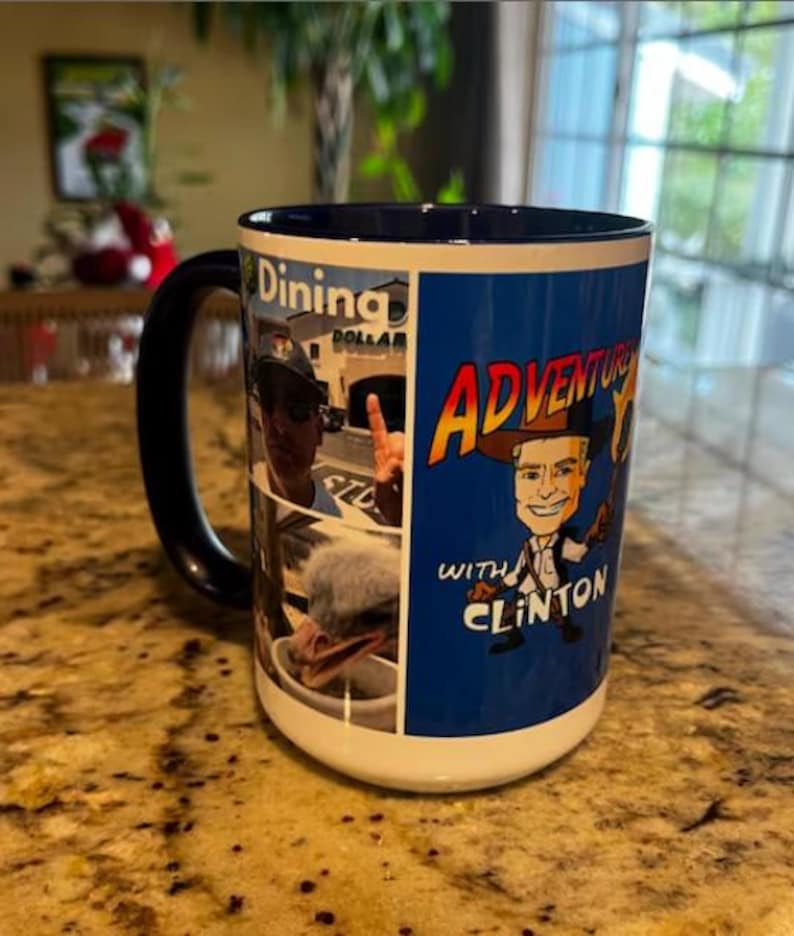 Puede incluir: Una taza de cer&aacute;mica grande con interior y asa azules. La taza presenta un collage de im&aacute;genes y las palabras "Dining Dollar" y "Adventures with Clinton" en un dise&ntilde;o colorido. La taza est&aacute; sobre una encimera moteada.