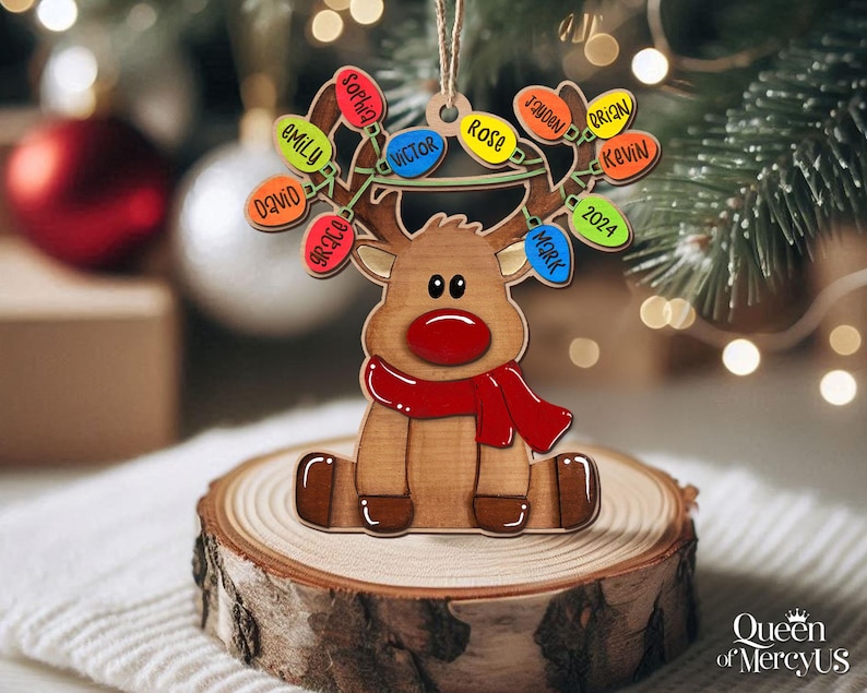 以下が含まれることがあります： 赤い鼻とスカーフが付いたトナカイの形をした木製のクリスマスオーナメント。トナカイには名前が書かれたカラフルなライトのストリングがあります。オーナメントは木の輪切りに置かれています。2024年もライトに表示されています。