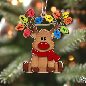 以下が含まれることがあります： 赤い鼻とスカーフが付いたトナカイの形をした木製のクリスマスオーナメント。トナカイは、名前が書かれたカラフルなライトの列を持っています。2024年もライトの一つに表示されています。オーナメントはクリスマスツリーに吊るされています。