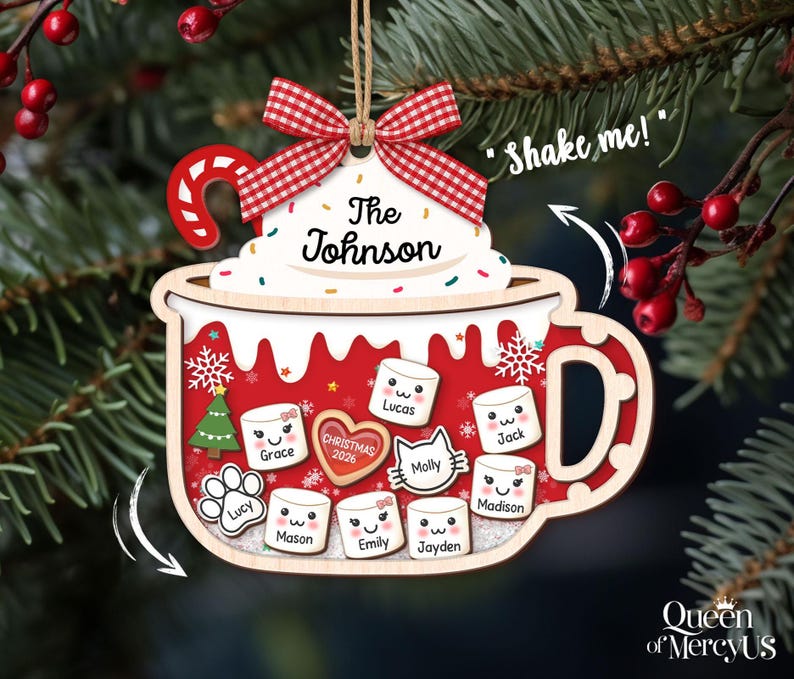 May include: A wooden Christmas ornament shaped like a mug filled with hot cocoa, featuring a red and white gingham bow, a candy cane, and white whipped cream labeled "The Johnson". The mug contains marshmallow-shaped charms with names.