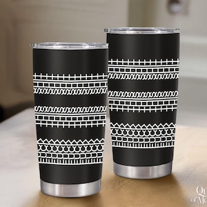 May include: Two black stainless steel tumblers with white geometric patterns. The designs include rows of crosses, X's, and other shapes. The tumblers have silver-colored bases and lids. The tumblers are on a wooden surface.