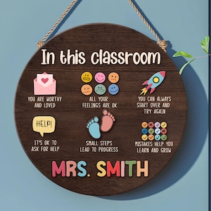 K&ouml;nnte beinhalten: Ein braunes, h&ouml;lzernes Klassenzimmer-Schild mit dem Text "In this classroom" und bunten Illustrationen und Text. Das Schild enth&auml;lt S&auml;tze wie "You are worthy and loved", "All your feelings are ok", "It's ok to ask for help", "Small steps lead to progress", "You can always start over and try again", "Mistakes help you learn and grow". Das Schild enth&auml;lt auch den Namen der Lehrerin, "MRS. SMITH".