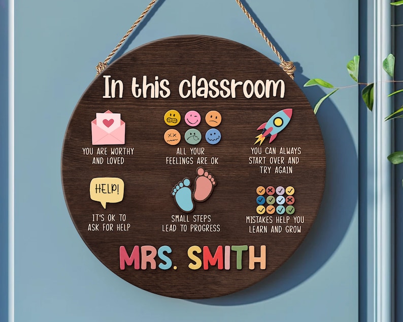 K&ouml;nnte beinhalten: Ein braunes, h&ouml;lzernes Klassenzimmer-Schild mit dem Text "In this classroom" und bunten Illustrationen und Text. Das Schild enth&auml;lt S&auml;tze wie "You are worthy and loved", "All your feelings are ok", "It's ok to ask for help", "Small steps lead to progress", "You can always start over and try again", "Mistakes help you learn and grow". Das Schild enth&auml;lt auch den Namen der Lehrerin, "MRS. SMITH".