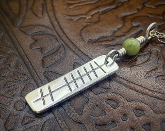 May include: A silver pendant with a series of etched lines, attached to a silver chain with a green stone bead.