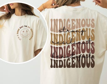 May include: Cream-colored t-shirt with the text "Indigenous" stacked vertically in a retro font, with the words "strong, resilient, beautiful" in between. The front of the shirt has a smiley face with the text "It's a good day to be Indigenous."
