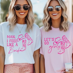 Puede incluir: Dos mujeres con gafas de sol y camisetas con gráficos de temática vaquera. Una camiseta es blanca con el texto "Man, I feel like a Bride" y la otra es rosa con "Let's go girls". Ambas camisetas presentan un sombrero y botas de vaquero.