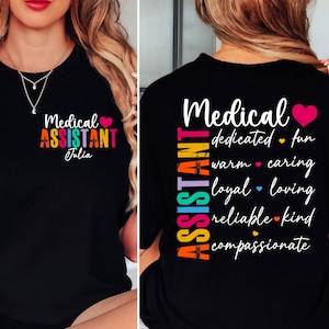 May include: Black t-shirt with the words "Medical Assistant" in colorful text and a pink heart. The name "Julia" is below the text. The back of the shirt has the words "Medical Assistant" and other words like "dedicated" and "caring".