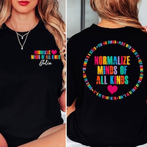 May include: Black t-shirt with the text "Normalize Minds of All Kinds" in colorful letters and a pink heart. The name "Julia" is written below the text. The back of the shirt has the same text in a circle.