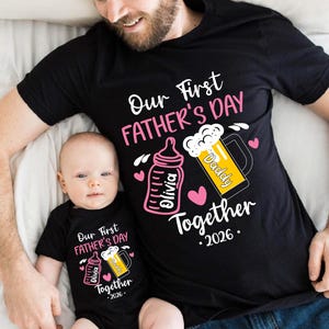 Może przedstawiać: Czarne koszulki z pasującymi wzorami dla ojca i dziecka. Koszulki mają napis "Our First Father's Day" i "Together 2026". Projekt zawiera butelkę dla dziecka, kufel piwa i imię "Olivia".