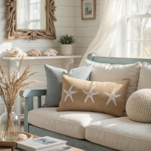 a cozy living room with a white sofa adorned with star-shaped throw pillows, a wooden coffee table, and a mirror on the wall. The room is decorated with a vase of dried flowers, a stack of books, and a potted plant, creating a warm and inviting atmosphere.