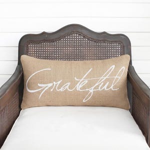 A wooden chair with a burlap pillow on it, featuring the word "gratitude" written on it.